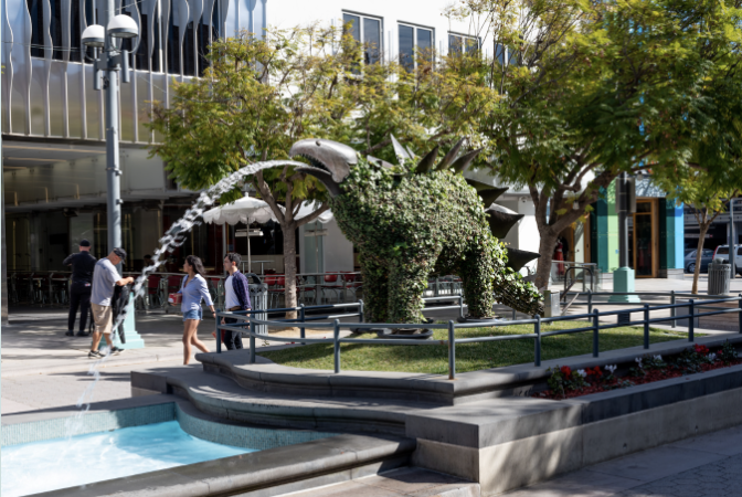 A large green dinosaur sculpture fountain placed outside in a common area.